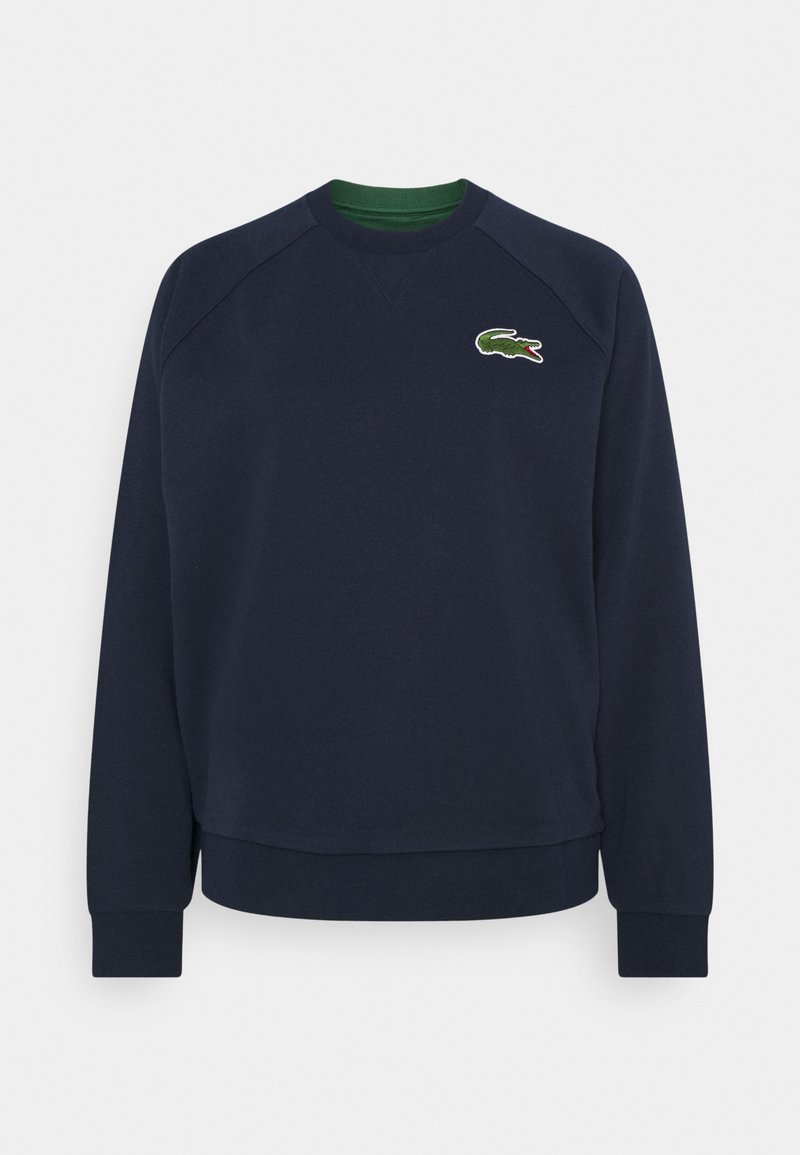 Sweat-shirt bleu marine avec manches raglan longues, poignets côtelés et encolure ronde. Présente un logo crocodile brodé en vert et blanc.