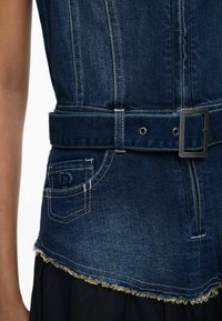 Denim vest with a dark wash, belted waist, textured frayed hem, and contrasting stitching. Includes a small pocket with decorative stitching.