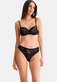 Ensemble de lingerie noire comprenant un soutien-gorge balconnet avec des bonnets en dentelle et armature, associé à un string taille haute assorti avec des accents en dentelle.