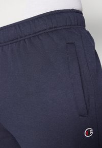 Námornícke modré tepláky vyrobené z jemnej bavlnenej zmesi, s elastickým pásom, bočnými vreckami a vyšitým logom na ľavom stehne.