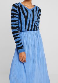 Blå stickad tröja med svarta ränder, V-halsdesign. Parat med en ljusblå plisserad kjol. Texturerat tyg ger visuell intresse.