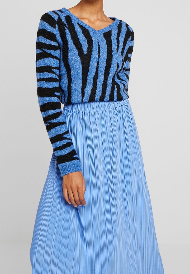 Blå stickad tröja med svarta ränder, V-halsdesign. Parat med en ljusblå plisserad kjol. Texturerat tyg ger visuell intresse.