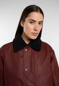 Bordeaux leren jas met een zwart fleece kraag, voorzien van drukknoopsluitingen en een gladde textuur. Close-up van het kraaggebied.