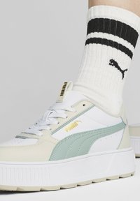 Bílé a světle mátové tenisky s robustní podrážkou, texturovanou kůží a zlatým logem. Nošeny s bílými ponožkami s žebrovaným vzorem a černými pruhy.