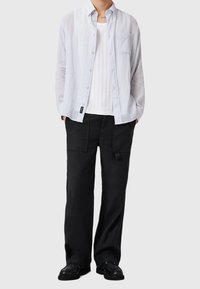 Vaaleansininen, raidallinen pitkähihainen pusero valkoisen ribbikankaisen tankotopin päällä. Yhdistetty löysästi istuviin mustiin cargo-housuihin ja mustiin kenkiin.