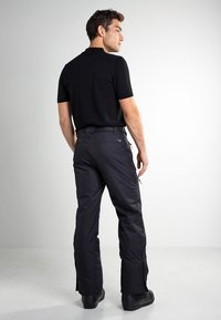 Chemise noire à manches courtes associée à un pantalon noir avec des zips aux chevilles, texture lisse et coupe ajustée.