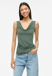 Top sans manches vert olive avec un col drapé et un détail froncé sur le côté, associé à un jean taille haute bleu clair. Texture du tissu lisse.