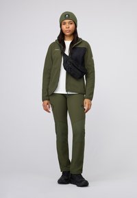 Olive green outdoor jacket with black accents, matching pants, and a black crossbody bag. Includes a fitted olive beanie. Durable materials.