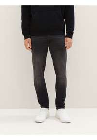 Tmavě šedé slim-fit džíny s jemným vyblednutím, pětipocketový design a zipový svršek, spárované s bílými teniskami a černou mikinou.