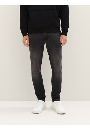 Dunkelgraue Slim-Fit-Jeans mit subtilen Ausbleichungen, Fünf-Taschen-Design und Reißverschluss, kombiniert mit weißen Sneakers und einem schwarzen Hoodie.