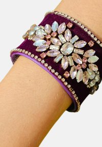 Bracelet en velours violet orné de grands rhinestones clairs et roses, présentant un design floral et des bords embellis de petites pierres.