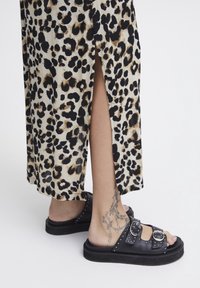 Sorte lædersandaler med to spænder og nitter. Båret med en leopardmønstret nederdel med en sideslids.
