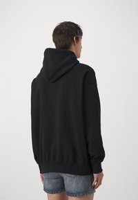 Zwarte hoodie met een trekkoord capuchon, geribbelde manchetten en zoom, met een zachte, gladde textuur. Draagbaar over denim shorts, getoond vanaf de achterkant.