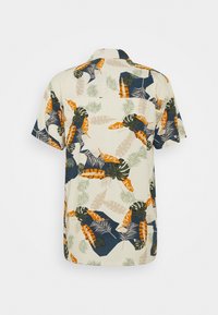 Camisa de manga corta con un fondo beige claro y un patrón de hojas tropicales en verde, naranja y azul marino. Diseño con cuello.