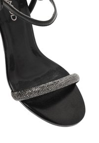 Sandal nero con tacco alto caratterizzato da una tomaia liscia, una sottile cinghia alla caviglia e una cinghia lucida decorata nella zona delle dita.