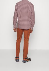 Röd och vit rutmönstrad långärmad skjorta, bruna byxor och svarta skor med oranga detaljer, sedd bakifrån.