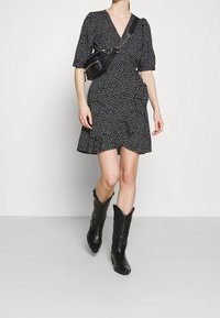 Musta kuvioitu kietaisumekko, jossa on lyhyet hihat ja reunus, yhdistettyinä mustiin cowboy-saappaisiin, joissa on monimutkaiset yksityiskohdat ja teräväkärkiset varret.