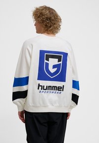 Vit sweatshirt med en stor grafisk design i blått och svart på baksidan, med blå och svarta ränder på ärmarna.