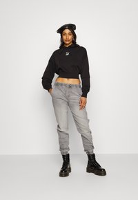 Svart cropped hettegenser med snor, grå joggebukser med elastiske mansjetter, og svarte klumpete snørestøvler. Hestepels-baret som aksent.