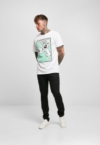 Maglietta bianca con una grafica colorata di Bugs Bunny su uno sfondo menta. Indossata con pantaloni neri e sneakers bianche.