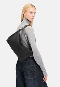 Czarna skórzana torba o zdefiniowanym kształcie, eleganckim designie i srebrnych elementach, noszona na ramieniu. Stylizowana z szarym golfem i ciemnymi dżinsami.