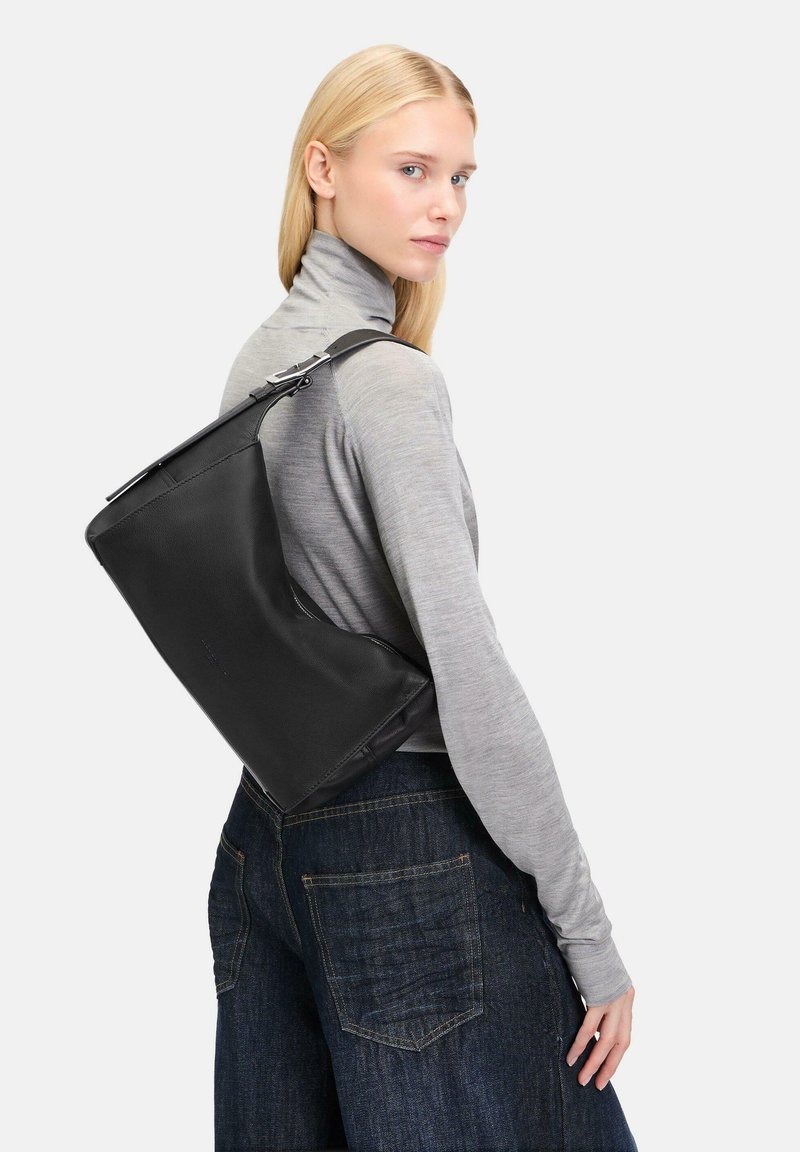 Czarna skórzana torba o zdefiniowanym kształcie, eleganckim designie i srebrnych elementach, noszona na ramieniu. Stylizowana z szarym golfem i ciemnymi dżinsami.