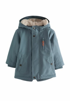 Giacca blu con cappuccio, foderata in crema texturizzata, bottoni a pressione, tasche laterali e un piccolo dettaglio in pelle nella zona della cerniera.