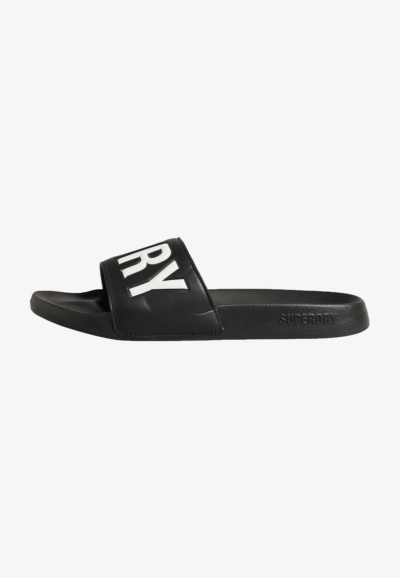 Sandale glissante noire en matériau synthétique, avec une large lanière portant l'inscription blanche "SUPERDRY" et un dessous de pied texturé pour une meilleure adhérence.