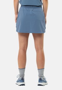 Lichtblauwe sportrok met een elastische tailleband, zijsplitdetail en gladde, lichte stof. Gekocht met grijze crew-sokken en blauwe sneakers.