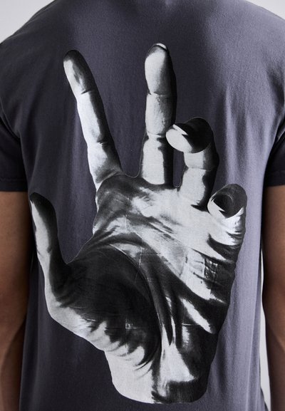 Black cotton t-shirt featuring a large, monochrome image of a hand making a peace sign on the back. Smooth texture, short sleeves.