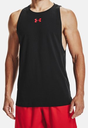 Mężczyzna ubrany w czarny bezrękawnik sportowy z czerwonym logo Under Armour i czerwone spodenki, stojący z rozluźnionymi ramionami.
