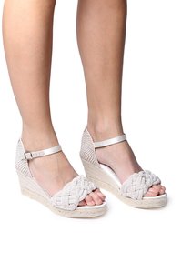 Sandalias de cuña con parte superior de tejido trenzado, color blanco, tira ajustable en el tobillo y suela de yute texturizada. Diseño de punta abierta.