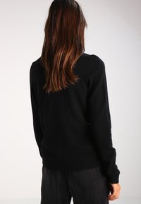 Černý pletený svetr s volným střihem, žebrovanými manžetami a lemem. Měkká textura s bezešvým zadním designem.