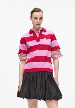 Red and pink striped polo shirt with a collared neckline and rolled sleeves, paired with a fitted black skirt.  Notable logo on the chest.
