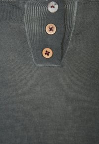 Grau Baumwoll-Henley-Shirt mit geripptem Kragen, drei Holzknöpfen mit roten Akzenten und strukturiertem Stoff.