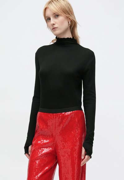 Top preto de mangas longas com um decote alto em forma de onda, combinado com calças brilhantes de lantejoulas vermelhas. O conjunto apresenta um ajuste justo e detalhes texturizados.