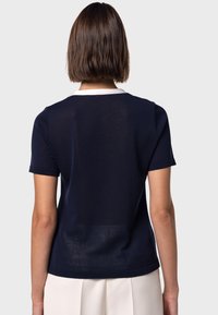 Marinblå kortärmad topp gjord av ett lätt strickad tyg, med en vit krage och en avslappnad passform, som har en slät yta.