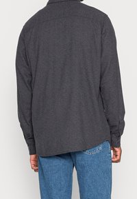 Ciemnoszara koszula z długim rękawem i kołnierzykiem, wykonana z teksturowanej tkaniny, z mankietami na guziki. Dół koszuli jest nieco dłuższy z tyłu.