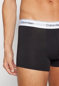 Čierne bavlnené boxerky s bielym elastickým pásom s logom "Calvin Klein", hladká textúra a priliehavý strih okolo stehien.
