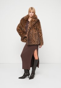 Kunstpelzmantel mit braunem und schwarzem Leopardenmuster, großem Kragen, kombiniert mit einem braunen, gerippten Kleid und kniehohen schwarzen Stiefeln.