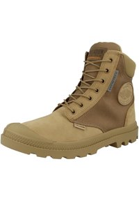 Bottine imperméable beige avec un dessus en suède et en mesh, semelle en caoutchouc robuste et œillets en métal avec des lacets ronds. Détail du logo sur le côté.