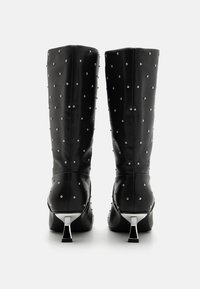 Mustad kuni põlve saapad, mis on valmistatud siledast materjalist, kaunistatud hõbedaste nupukestega, kondiga vormitud kontsaga, mille aluses on metalliline aktsent.