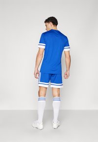 Blå atletisk tröja med vita och blå randiga detaljer, i kombination med matchande shorts, vita knähöga strumpor och fotbollsskor.