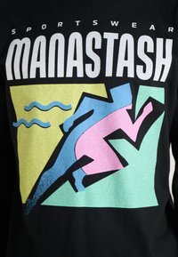 Black T-shirt featuring vivid graphic design with the word "MANASTASH" and abstract sports figures in pink, blue, green, and yellow shapes.