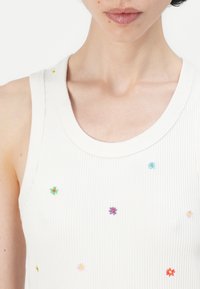 Witte geribde tanktop met een ronde halslijn, voorzien van een multikleurige bloemenborduring verspreid over de stof.