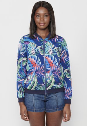 Veste bombers florale en bleu, ornée de motifs de feuilles tropicales vibrants en vert, rose et violet ; poignets et ourlet côtelés ; fermeture à glissière à l'avant.