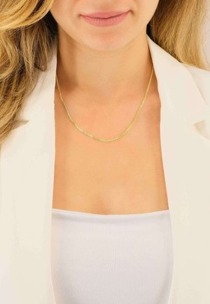 Goldene Halskette mit einem zarten Design aus flachen Gliedern, getragen über einem weißen Oberteil und kombiniert mit einem hellen Blazer.