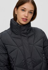 Chaqueta de abrigo acolchada negra con un alto cuello, costuras geométricas y una textura suave. Diseño ligero adecuado para el clima frío.