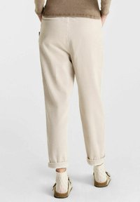 Beige corduroy broek met een losse pasvorm, omgeslagen bij de enkels, met verticale ribbels en gedragen met lichte, gebreide sokken en sandalen.