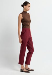 Bruine geribbelde mouwloze top, gecombineerd met hoog-waist, op maat gemaakte bordeauxrode broeken. Bruine gestructureerde schoenen met lage hakken maken de outfit compleet.